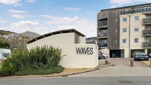 A building labeled 'WAVES' with a parking area and a road in front. - 1 bedroom accommodation in Newquay (Newquay)