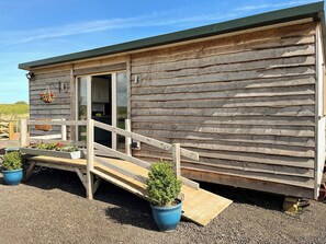 Eine Holzhütte mit einer Holztreppe, die zu einer Tür führt, einer kleinen Veranda mit Topfpflanzen und einem Kiesweg.