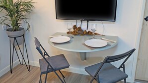 A dining area with a round table, two chairs, a potted plant, and a flat-screen TV mounted on the wall. - Raygill Shepherds Hut (Dishforth, near Thirsk)