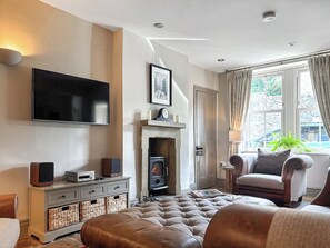 Una sala de estar con televisor de pantalla plana, chimenea, sofá de cuero, sillón y un ventanal con cortinas.