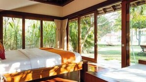 A bedroom with a large bed, wooden headboard, and a view of a garden through large windows.