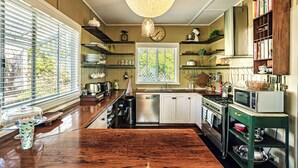 A kitchen with wooden countertops, a stainless steel dishwasher, a stove, and a microwave. There are shelves with dishes and a clock on the wall. - Charming 1940's two bedroom cottage, established gardens, large verandah and BBQ (Dorrigo)