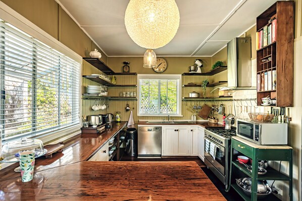 A kitchen with wooden countertops, a stainless steel dishwasher, a stove, and a microwave. There are shelves with dishes and a clock on the wall.