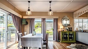 A dining area with a table, chairs, and a patterned rug. There is a green cabinet with glass doors and a mirror above it. - Charming 1940's two bedroom cottage, established gardens, large verandah and BBQ (Dorrigo)