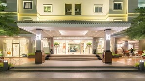 Entrada de hotel con una galería techada, escalones que conducen a la entrada y plantas en macetas.