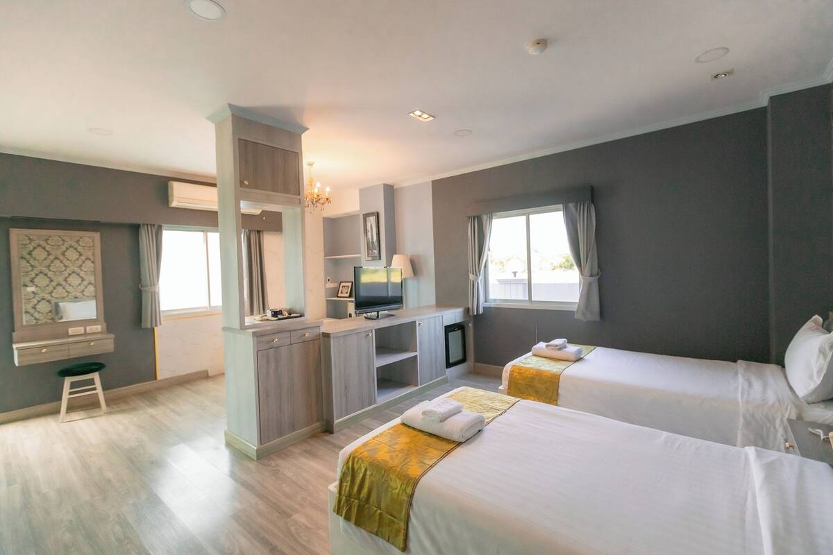 Ein Hotelzimmer mit zwei Betten, einem Schreibtisch, einem Fernseher und einer kleinen Küchenzeile.