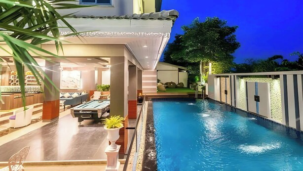 Una piscina con mesa y sillas, un área al borde de la piscina y un edificio con tejado de azulejos.