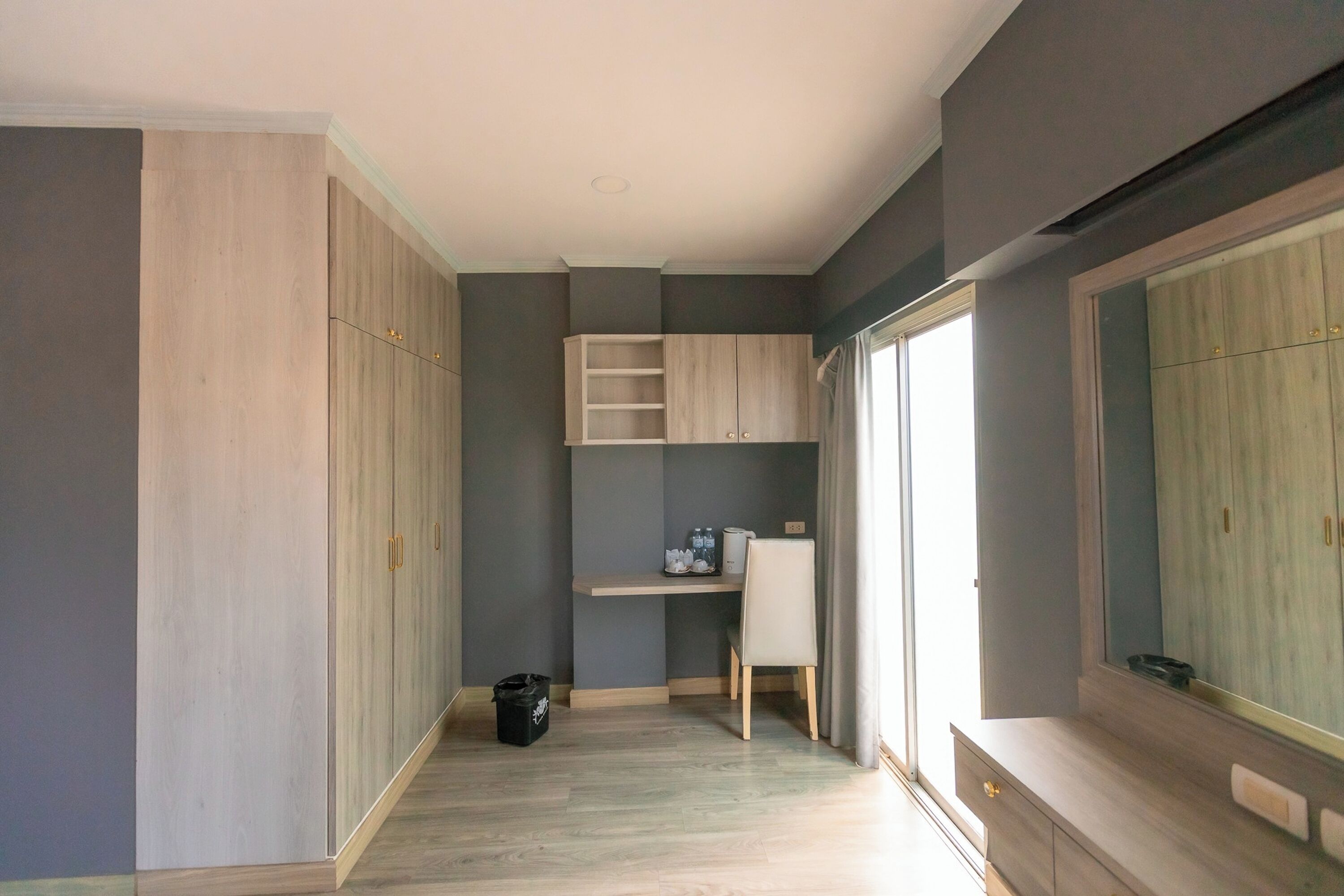 A room with a desk, wardrobe, and a large mirror.