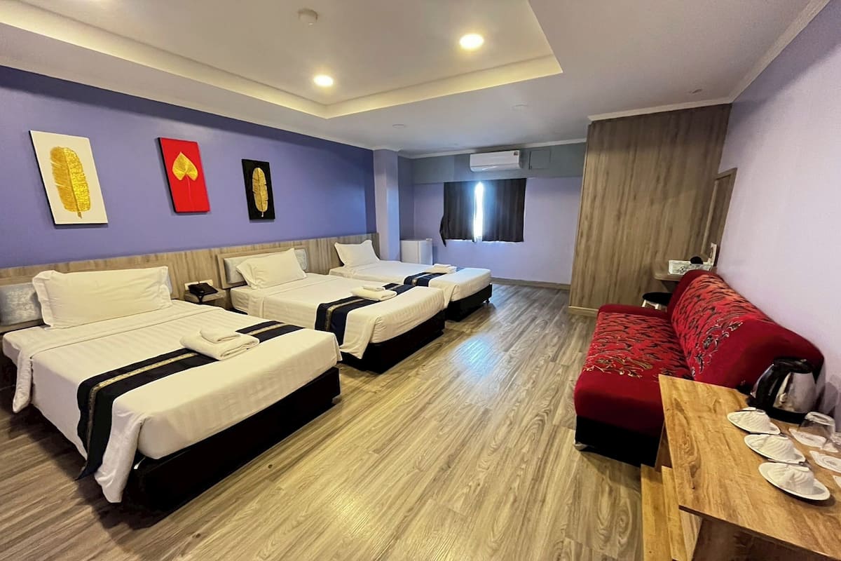 Ein Hotelzimmer mit drei Betten, einem roten Sofa, einem Holztisch und Kunstwerken an der Wand.
