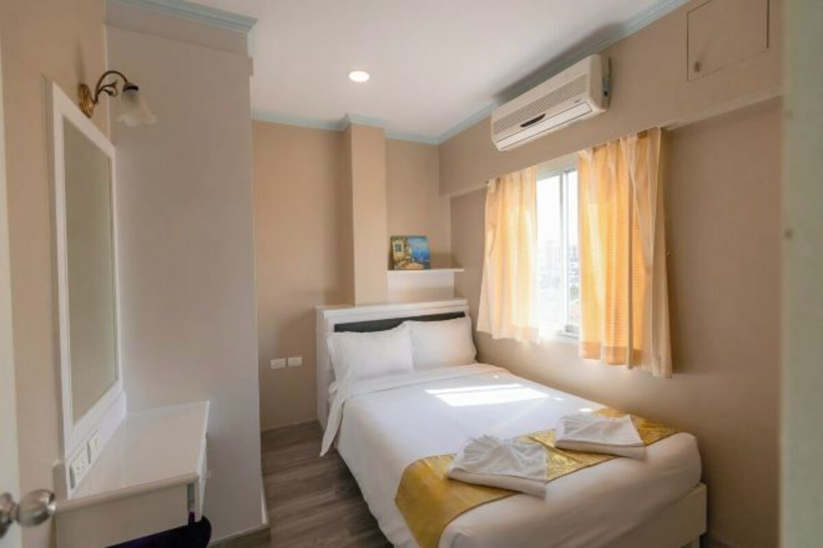 Une chambre d’hôtel comprenant un lit, une table de chevet, un miroir, une fenêtre avec des rideaux et un appareil de climatisation.