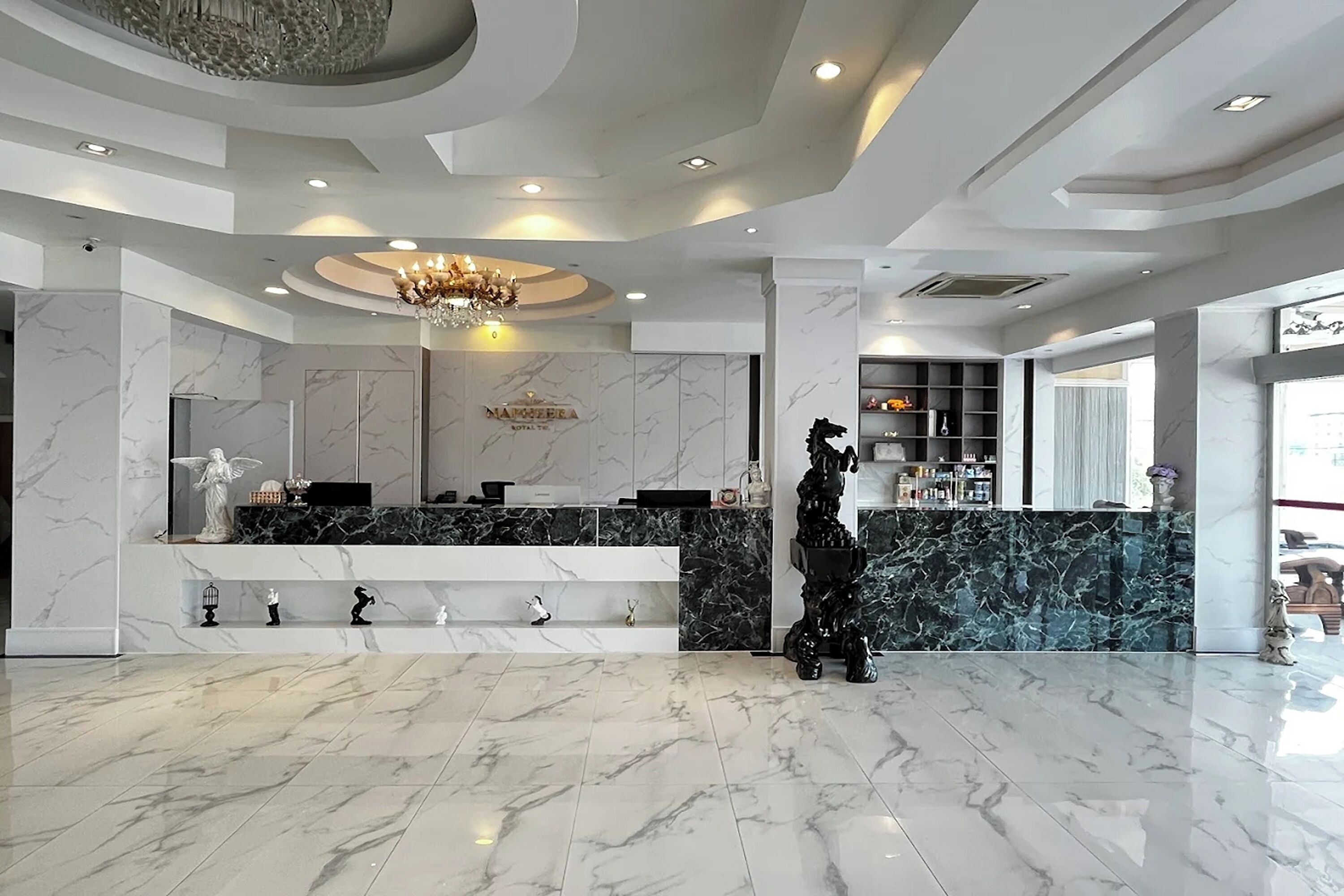 Un vestíbulo de hotel con un mostrador de recepción de mármol, un candelabro y una estatua.