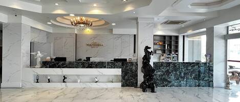 Un vestíbulo de hotel con un mostrador de recepción de mármol, un candelabro y una estatua.