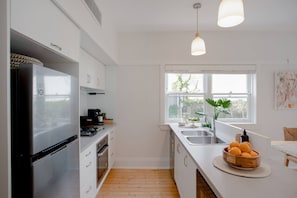 A modern kitchen with white cabinetry, a stainless steel refrigerator, a sink, and a window with a view of greenery.