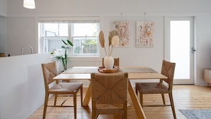 Uma sala de jantar moderna com uma mesa de madeira, cadeiras de palha e um vaso com flores secas.