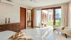 Un dormitorio amplio con una cama grande, un ventilador de techo y vistas a un área exterior ajardinada a través de un ventanal corredero.