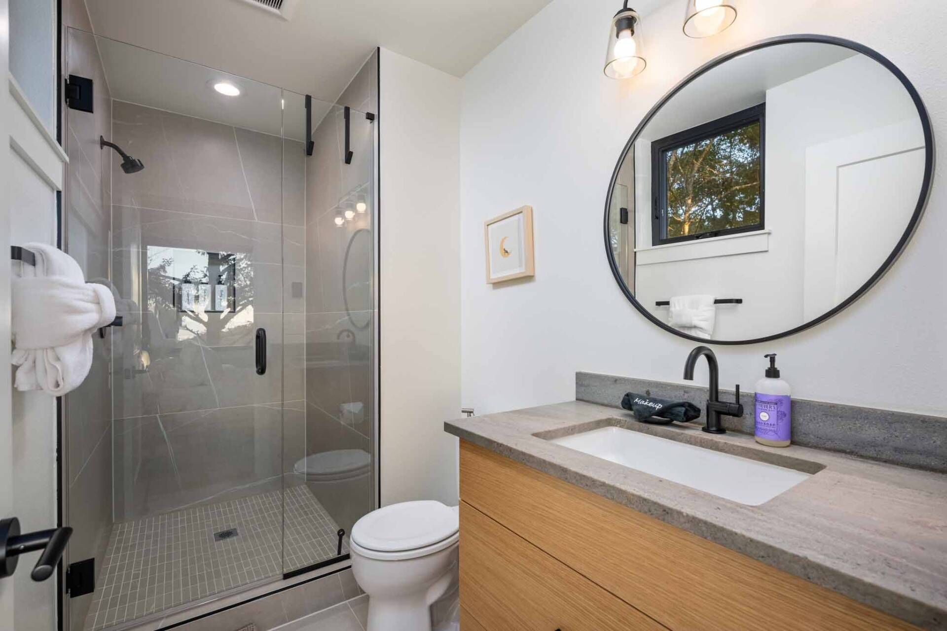 A modern bathroom with a glass-enclosed shower, a white toilet, a vanity with a sink, and a large mirror.