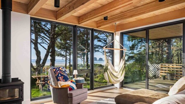 A cozy living room with a large window, a hammock, a fireplace, and a view of the ocean. - CoHo Vista: Curated Comfort, High-End Style & Breathtaking Coastal Views, Seconds Away From Beach (Rockaway Beach)