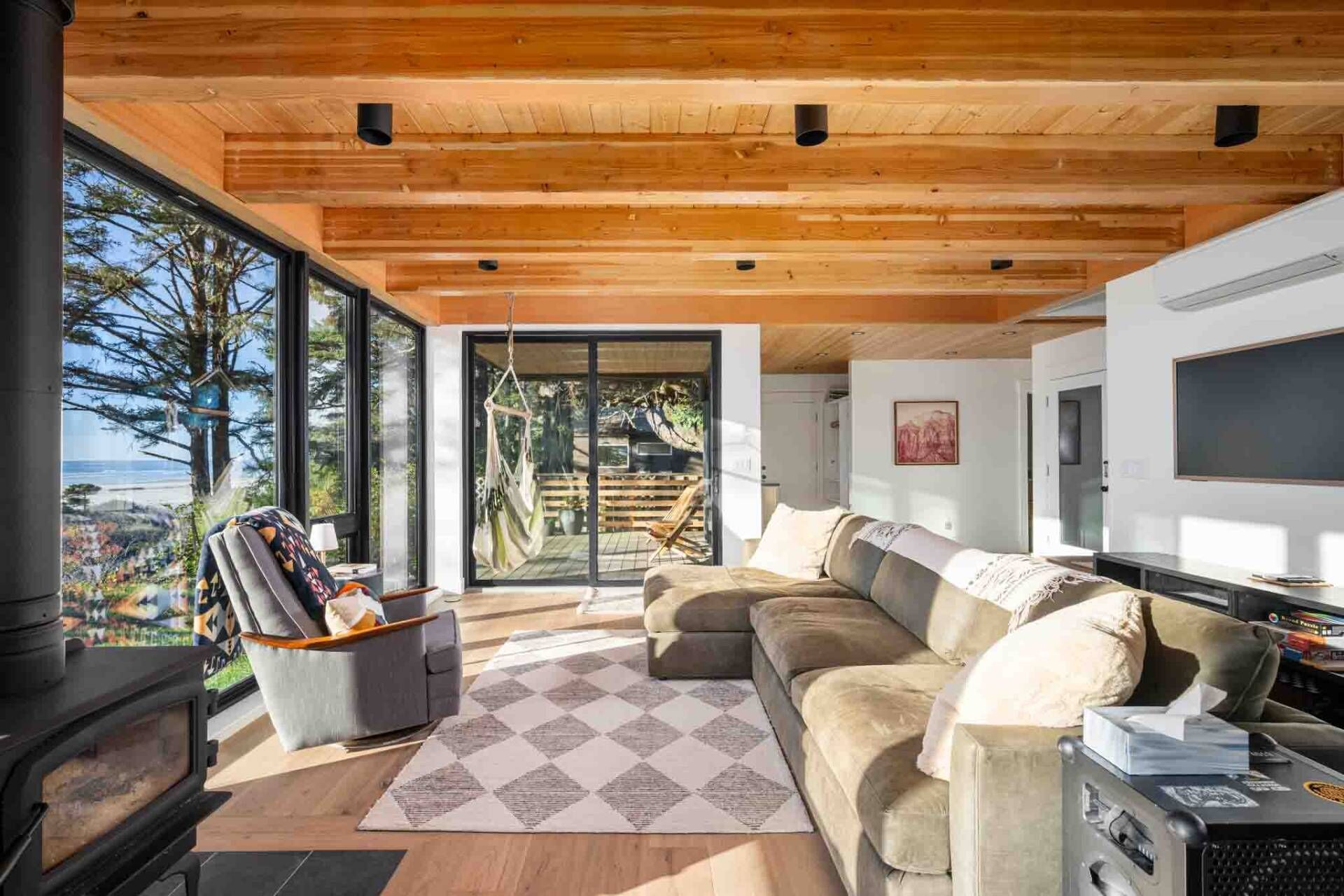 A modern living room with a wooden ceiling, a large window offering a view of the outdoors, a sofa, a TV, and a fireplace.