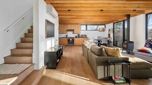 A modern interior with a wooden staircase, a living area with a sofa, a dining table, and a kitchen area. - CoHo Vista: Curated Comfort, High-End Style & Breathtaking Coastal Views, Seconds Away From Beach (Rockaway Beach)