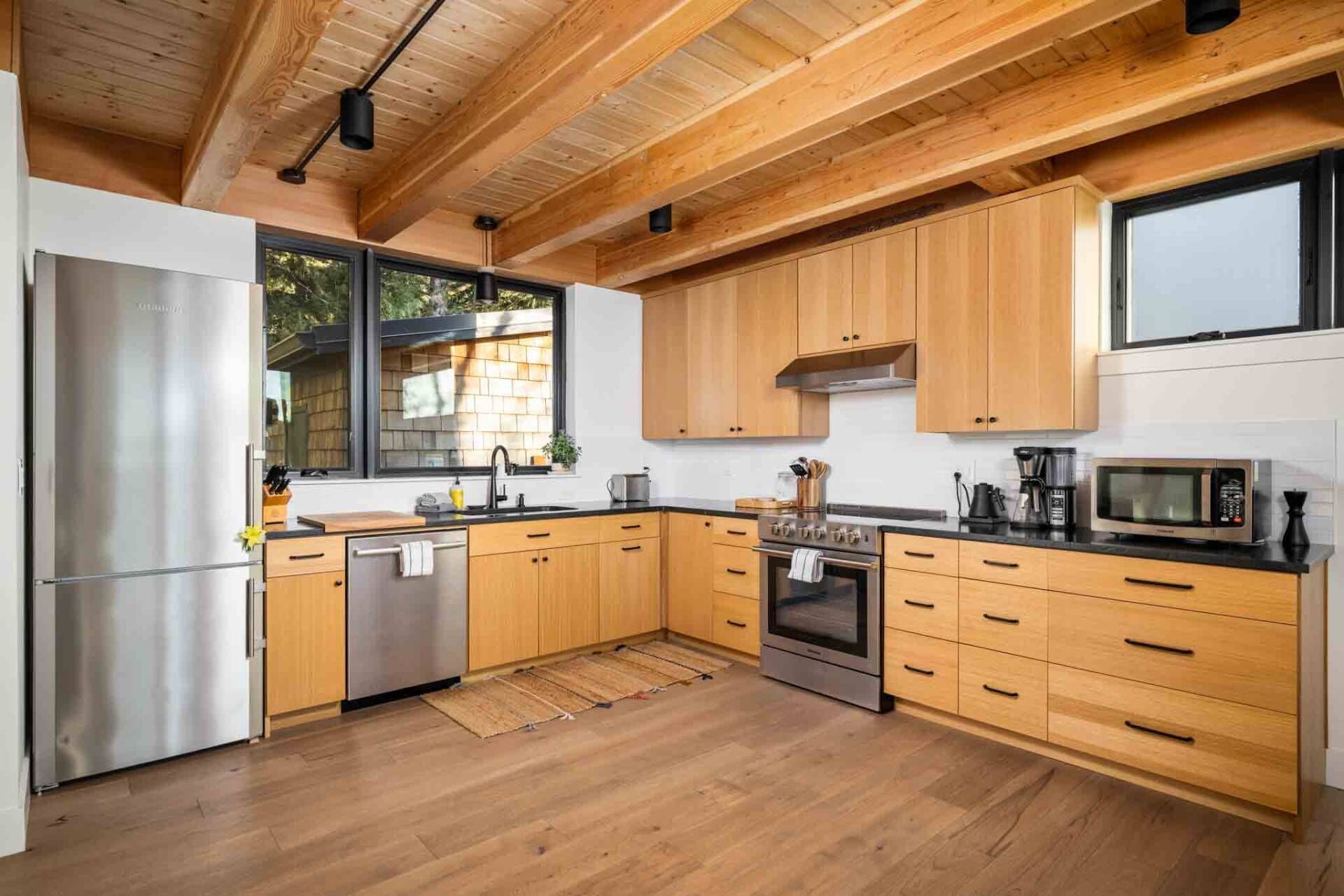 Une cuisine moderne dotée de meubles en bois, d’appareils électroménagers en acier inoxydable et d’une grande fenêtre qui laisse entrer la lumière naturelle.