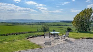 Paesaggio rurale con patio sterrato, due sedie in metallo e un tavolo.