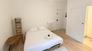 A bedroom with a bed, a wooden nightstand, a white radiator, and a door. - Studio Paris 15ème: Proche Métro Parfait pour 2 (Paris)