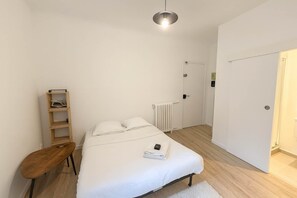 A bedroom with a bed, a wooden nightstand, a white radiator, and a door.