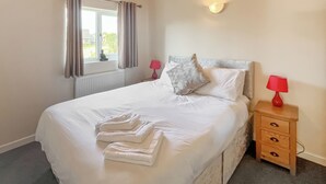 A neatly made bed with folded towels, a bedside table with a lamp, and a window with curtains. - 3 bedroom accommodation in Brigg (Brigg)