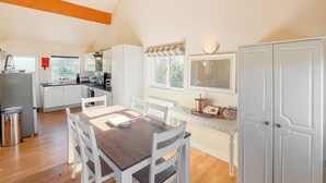 A modern kitchen with white cabinets, a dining table with white chairs, and a view of the outdoors through a window. - 3 bedroom accommodation in Brigg (Brigg)