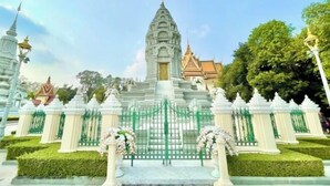 A temple with a central stupa, surrounded by a white fence and green gates, with a clear sky above. - SKY Apartments - 50m to National Museum (Phnom Penh)