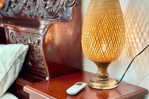 Une lampe avec un abat-jour texturé, posée sur une table en bois à côté d’un lit doté d’une tête de lit.
