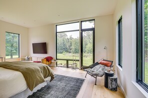 A spacious bedroom with a large bed, a seating area with a view, and a television mounted on the wall. - Hudson Valley Summer Escape w/ Pool & Fire Pit (Pine Plains)