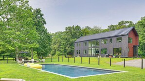 Una casa moderna con piscina, rodeada de césped cuidado y árboles.