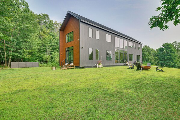 A modern two-story house with a large front yard, wooden deck, and outdoor seating area. - Hudson Valley Summer Escape w/ Pool & Fire Pit (Pine Plains)