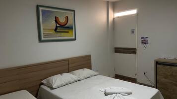 A hotel room with a bed, a headboard, a painting, a mirror, and a desk with a computer.