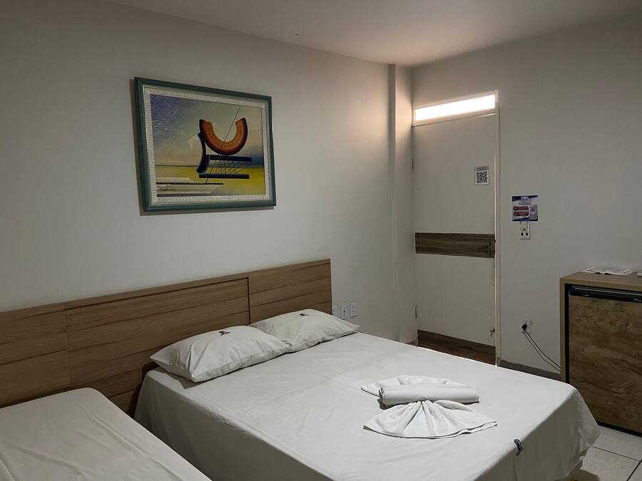 A hotel room with a bed, a headboard, a painting, a mirror, and a desk with a computer.