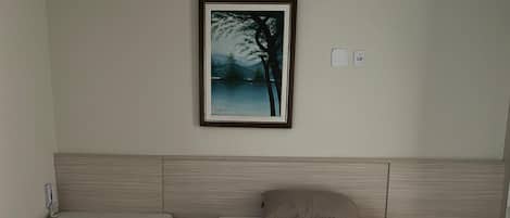 Habitación de hotel con cama, mesita de noche, un cuadro colgado en la pared y un enchufe.