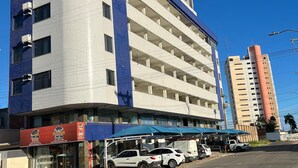 A multi-story hotel with a blue and white facade, a covered parking area, and several parked cars. - Kris Hotel (Petrolina)