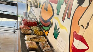 A buffet with various food items like bread, pastries, and nuts, and a wall with a colorful mural. - Kris Hotel (Petrolina)