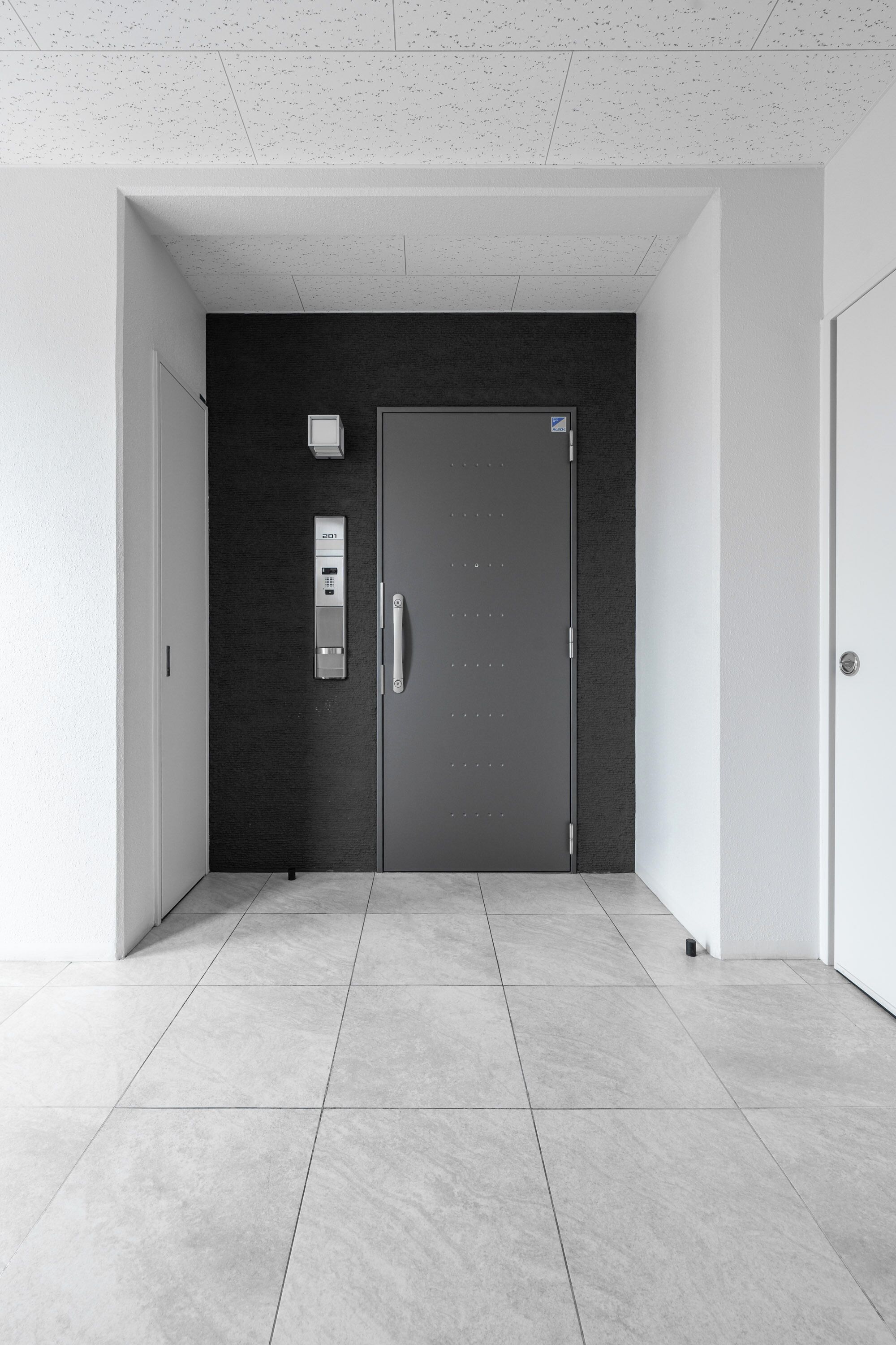 A modern hallway with a dark wall, a door with a handle, and a control panel on the wall.