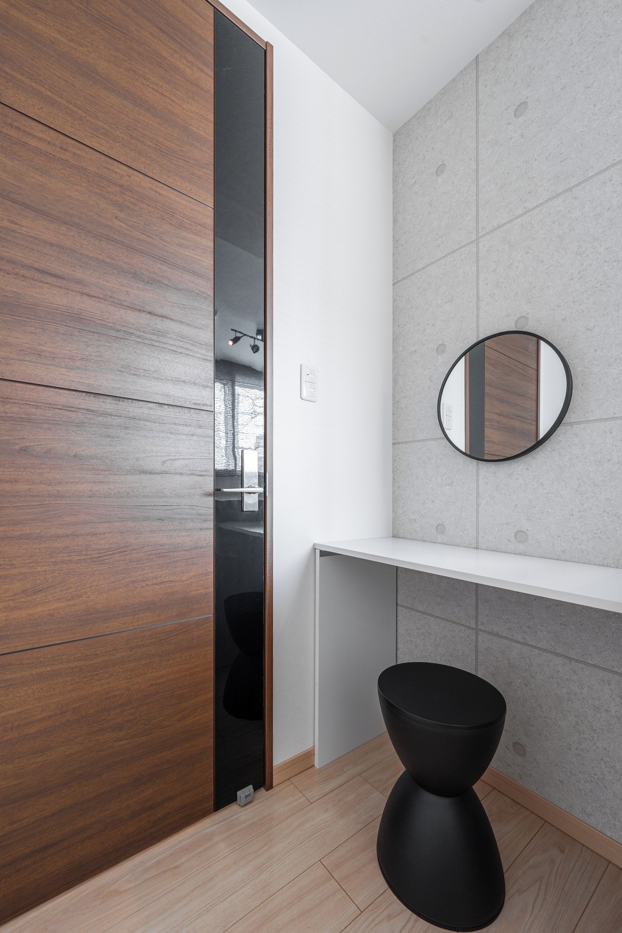A modern bathroom with a wooden vanity, a round mirror, and a black stool.