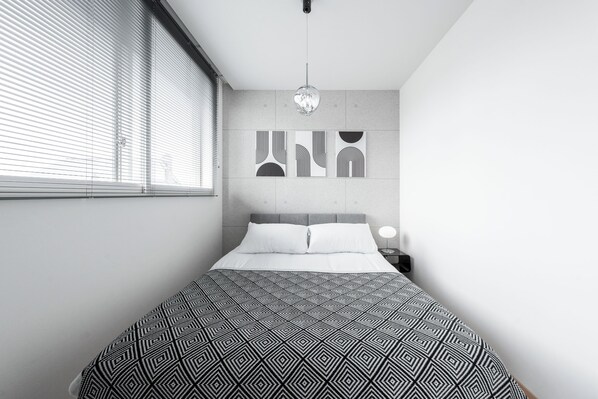 A modern bedroom with a geometric-patterned bedspread, a headboard, and abstract wall art.
