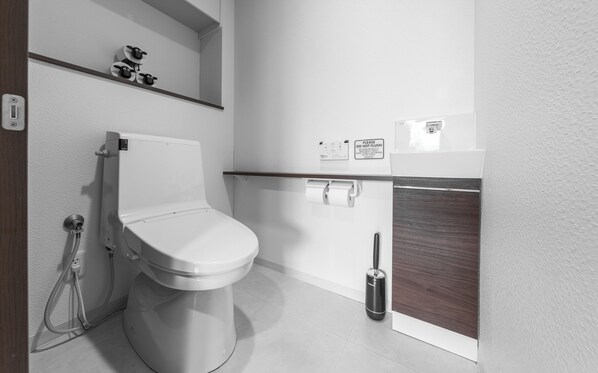 A modern bathroom with a toilet, a shower, and a bidet. There is a shelf with decorative items above the toilet.