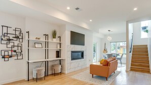 A modern living room with a fireplace, wooden flooring, a sofa, and a staircase leading to another level.