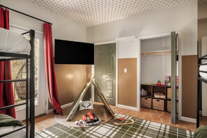 Kinderzimmer mit Etagenbetten, einem Flachbildfernseher, einem Kleiderschrank und einem Spielbereich mit Spielzeug.