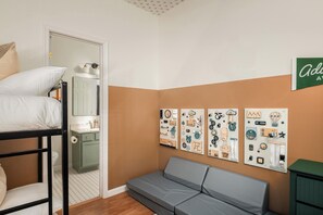 Ein Zimmer mit Etagenbett, einer kleinen Küchenzeile, einem grauen Sofa und Wandbildern.