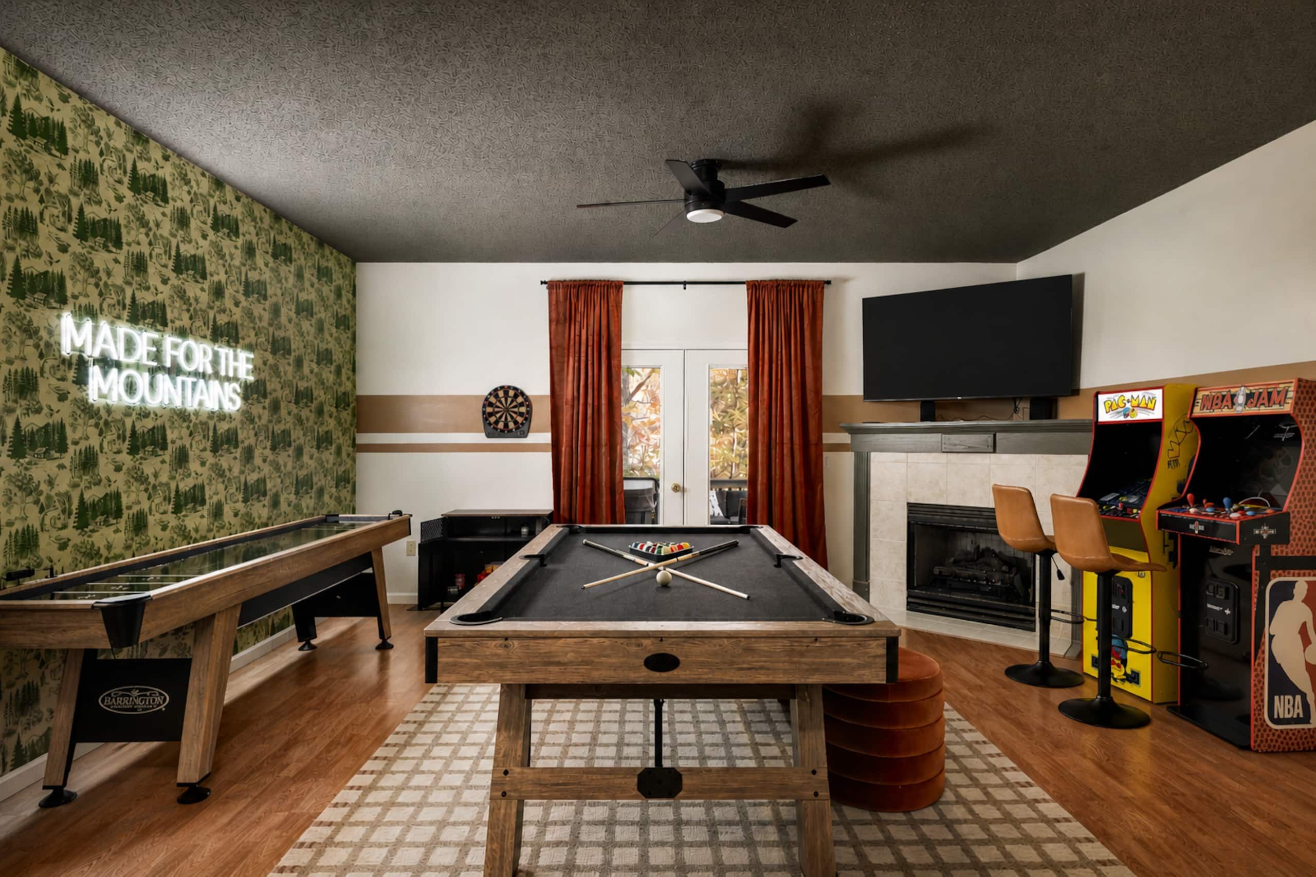 A room with a pool table, dartboard, and arcade games.