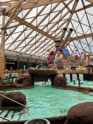 An indoor water park with a large transparent roof, slides, and a play area.