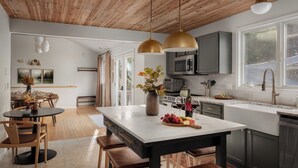 A modern kitchen with a wooden ceiling, a central island with seating, and a large window providing natural light.