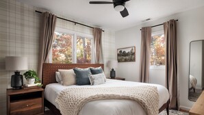A bedroom with a large bed, two bedside tables, a ceiling fan, and a window with curtains.